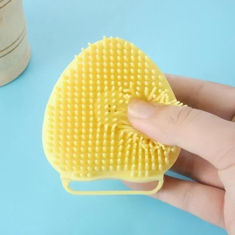 Yellow silicone face cleaning brush for pets held by a hand on a blue background